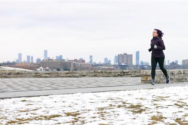 A woman jogging on a snowy path with a city skyline in the background