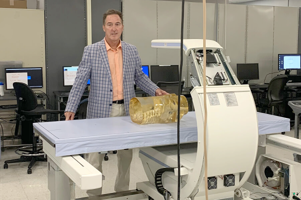 Man in blue jacket stand behind a medical device. 
