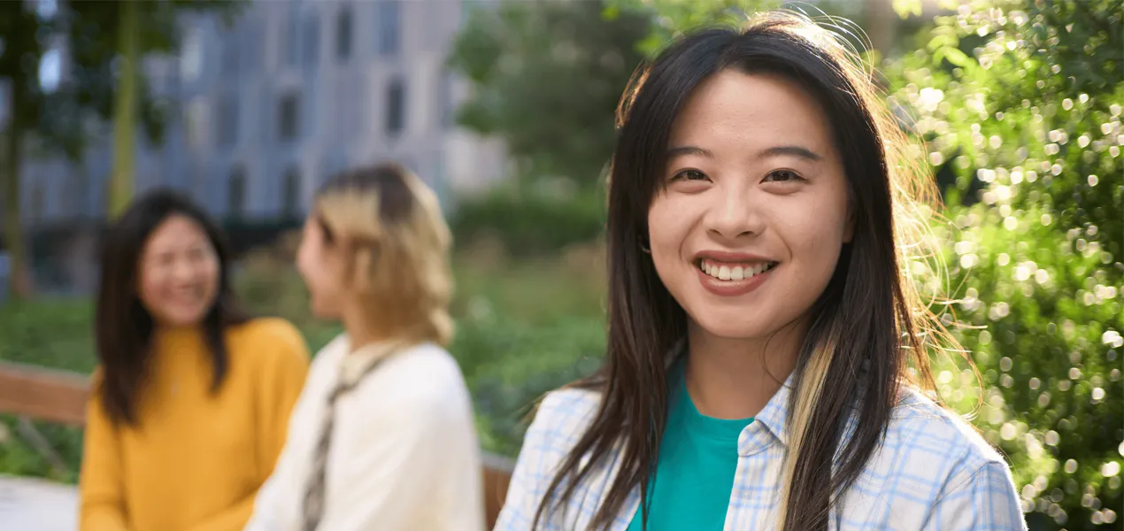 Young asian women smiling at the front of the photo with two women sitting on the bench behind her out of focus